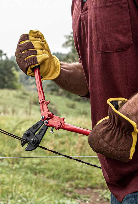 A farm hand wearing Work n’ Sport leather work gloves cuts a fense wire with wirecutters.